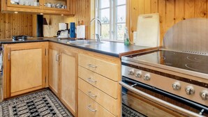 A kitchen with wooden cabinets, a stainless steel stove, and a window providing natural light. - 6 Person Holiday Home in Rodvig Stevns (Rodvig Stevns)