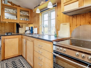 A kitchen with wooden cabinets, a stainless steel stove, and a window providing natural light. - 6 Person Holiday Home in Rodvig Stevns (Rodvig Stevns)