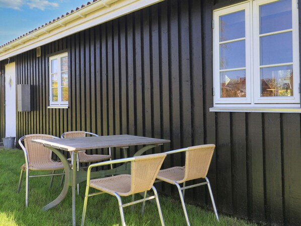 A building with a dark exterior, a window with a white frame, and a table with chairs outside.