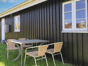 A building with a dark exterior, a window with a white frame, and a table with chairs outside. - 6 Person Holiday Home in Rodvig Stevns (Rodvig Stevns)