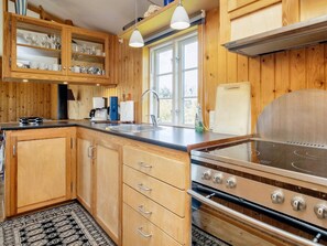A kitchen with wooden cabinets, a stainless steel stove, a sink, and a window with a view. - 6 Person Holiday Home in Rodvig Stevns (Rodvig Stevns)