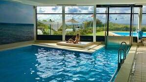 A pool area with a view of the sea and a person relaxing on a sun lounger. - Lovely Apartment in Neustadt (Neustadt in Holstein)