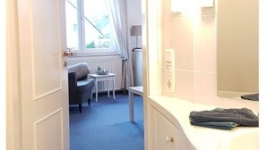 Ein Hotelzimmer mit Bad, Schreibtisch, Stuhl und Fenster.