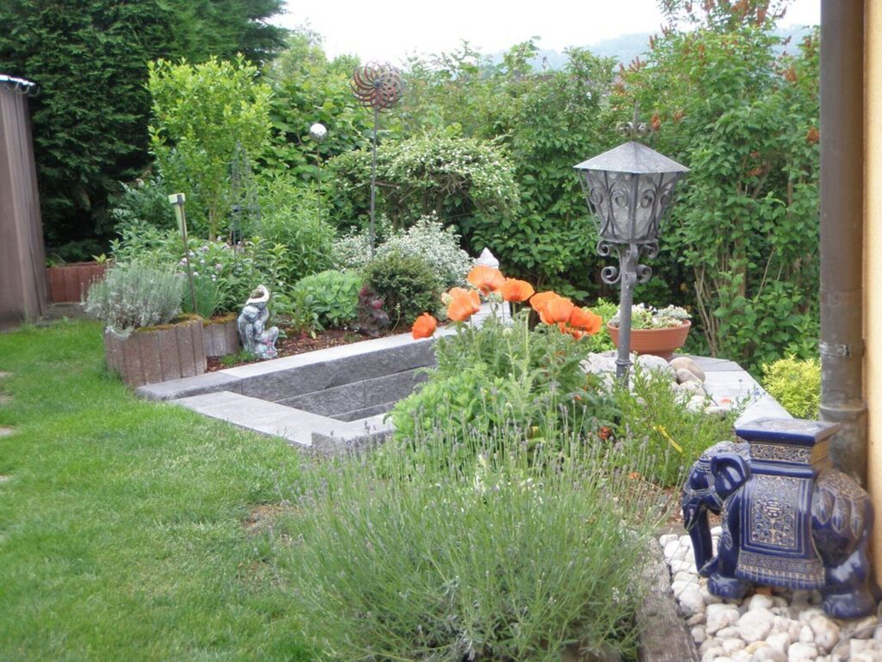 A garden with a variety of plants, a decorative statue, and a traditional lantern.