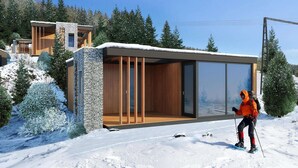 A modern ski lodge with a stone exterior, large glass windows, and a wooden deck.