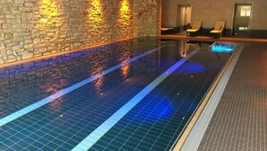 A swimming pool with stone walls and a tiled floor, surrounded by lounge chairs and a door. - Postwiese Comfortable Holiday Residence (Winterberg)