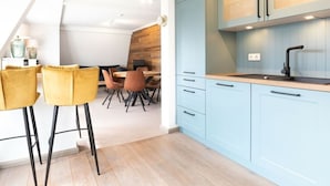A modern kitchen with light blue cabinets, a wooden dining table, and two yellow bar stools. - Penthuus Modern Retreat (Juist)