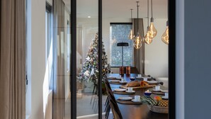 A modern dining area with a Christmas tree, a long table set for a meal, and hanging light fixtures. - Modern Koksijde Villa by Sea (Koksijde)