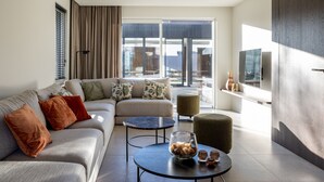 A modern living room with a sofa, two round coffee tables, and a large window with curtains. - Modern Koksijde Villa by Sea (Koksijde)
