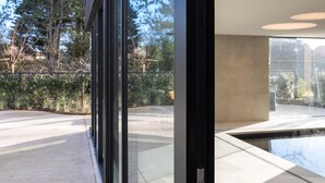 A modern building with large glass windows, a concrete interior, and a view of trees and mountains. - Modern Koksijde Villa by Sea (Koksijde)