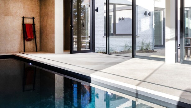 A modern indoor pool area with clear glass doors leading to an outdoor patio. - Modern Koksijde Villa by Sea (Koksijde)