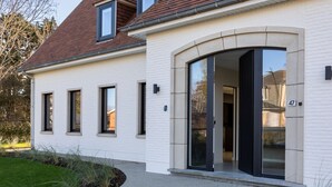 A modern house with a white exterior, a brown roof, and a large sliding glass door. - Modern Koksijde Villa by Sea (Koksijde)