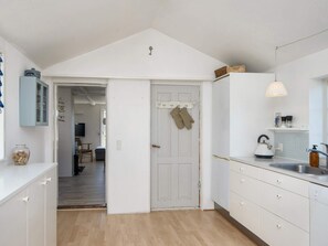 Une cuisine avec des meubles blancs, un plancher en bois, un luminaire suspendu et une porte dotée d’un trou de serrure.