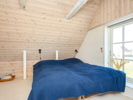 Un dormitorio con techo inclinado, cama con cubrecama azul, ventana con vistas y suelo de madera.