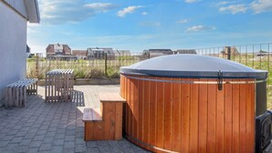 A wooden hot tub with a bench and a table, set on a paved patio with a view of houses in the background. - 10 Person Holiday Home in Harboore (Harboore)