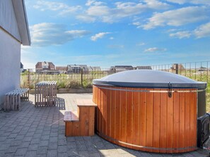 A wooden hot tub with a bench and a table, set on a paved patio with a view of houses in the background. - 10 Person Holiday Home in Harboore (Harboore)