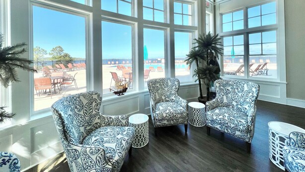 Una habitación con ventanas amplias, sillas con estampado y vista a una piscina y una playa.