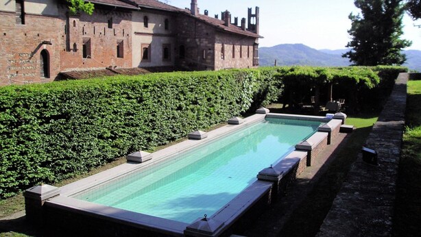 A pool adjacent to a historic building with a stone facade and arched windows. - Apartment in a Famous Monferrato Castle (Gabiano)