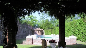 An outdoor dining area with a table set for tea, a pool in the background, and a stone wall. - Apartment in a Famous Monferrato Castle (Gabiano)