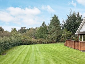 A well-maintained lawn with a wooden fence and a house with a gabled roof.