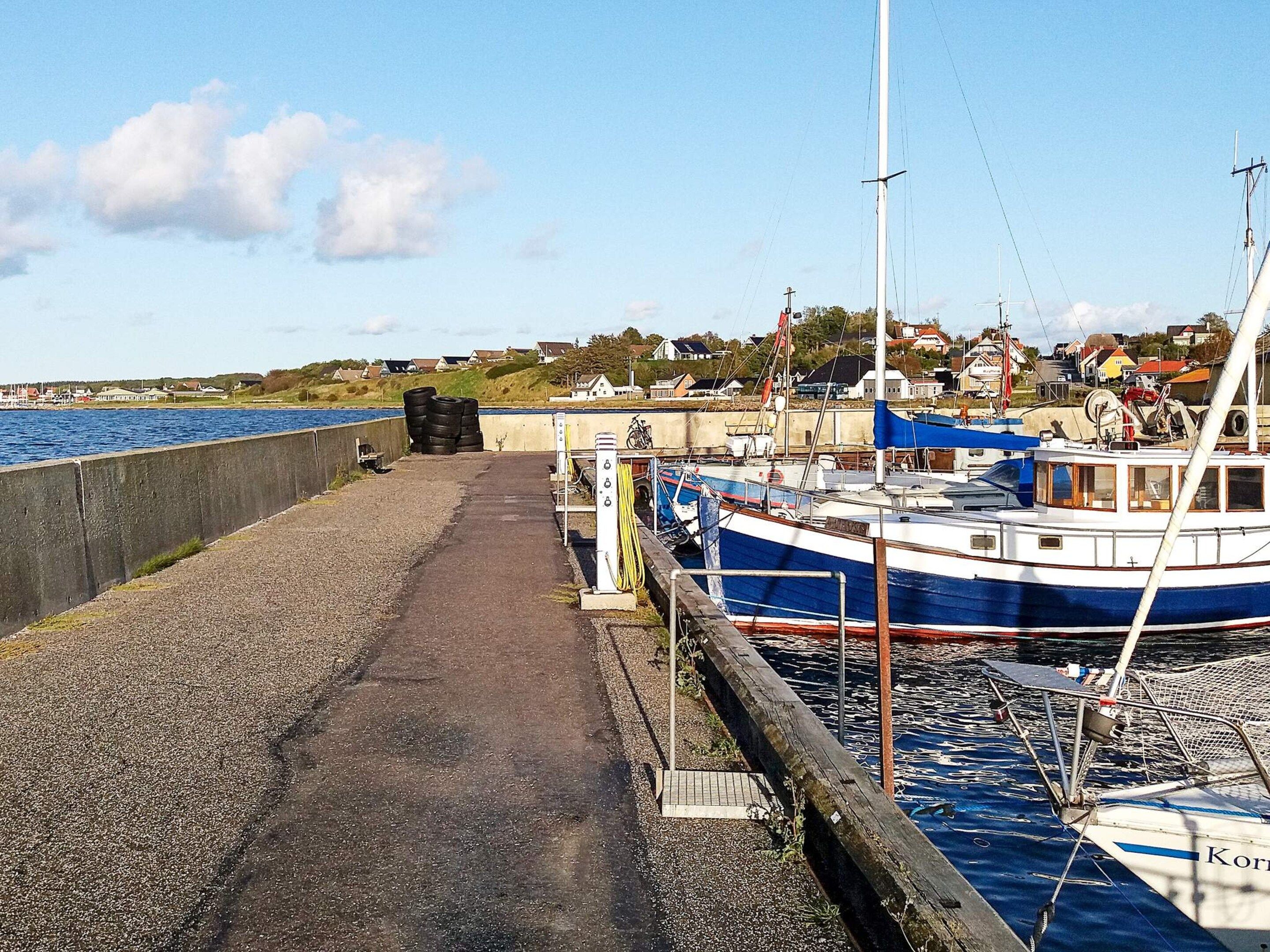 A harbor with boats docked, a concrete walkway, and houses in the background.