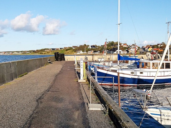 Un port avec des bateaux amarrés, une promenade en béton et des maisons en arrière-plan.