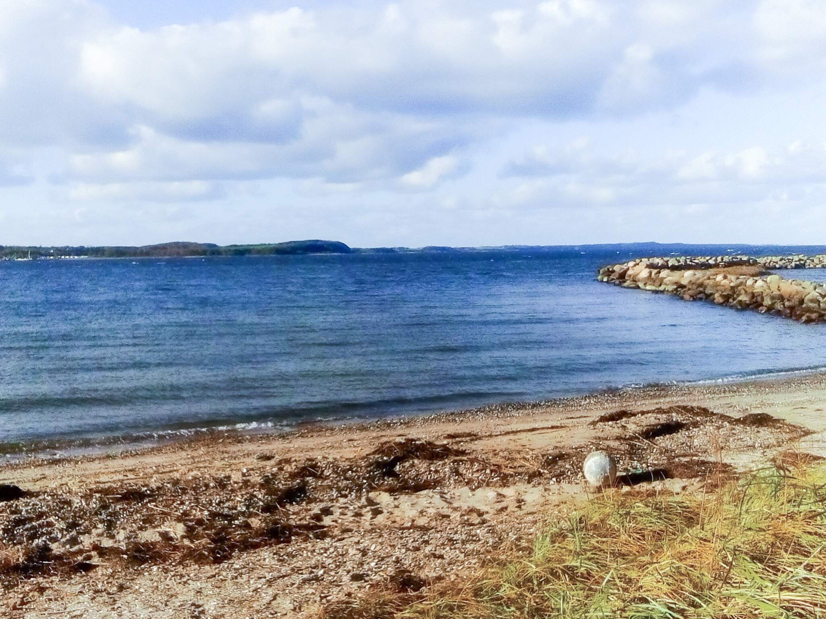 Ein Küstenstrand mit felsigem Ufer, blauem Himmel und weit entfernten Landformen.