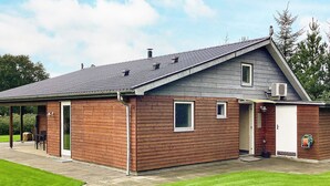 Een gebouw met twee verdiepingen, een schuin dak, een overdekt terras en een kleine garage.