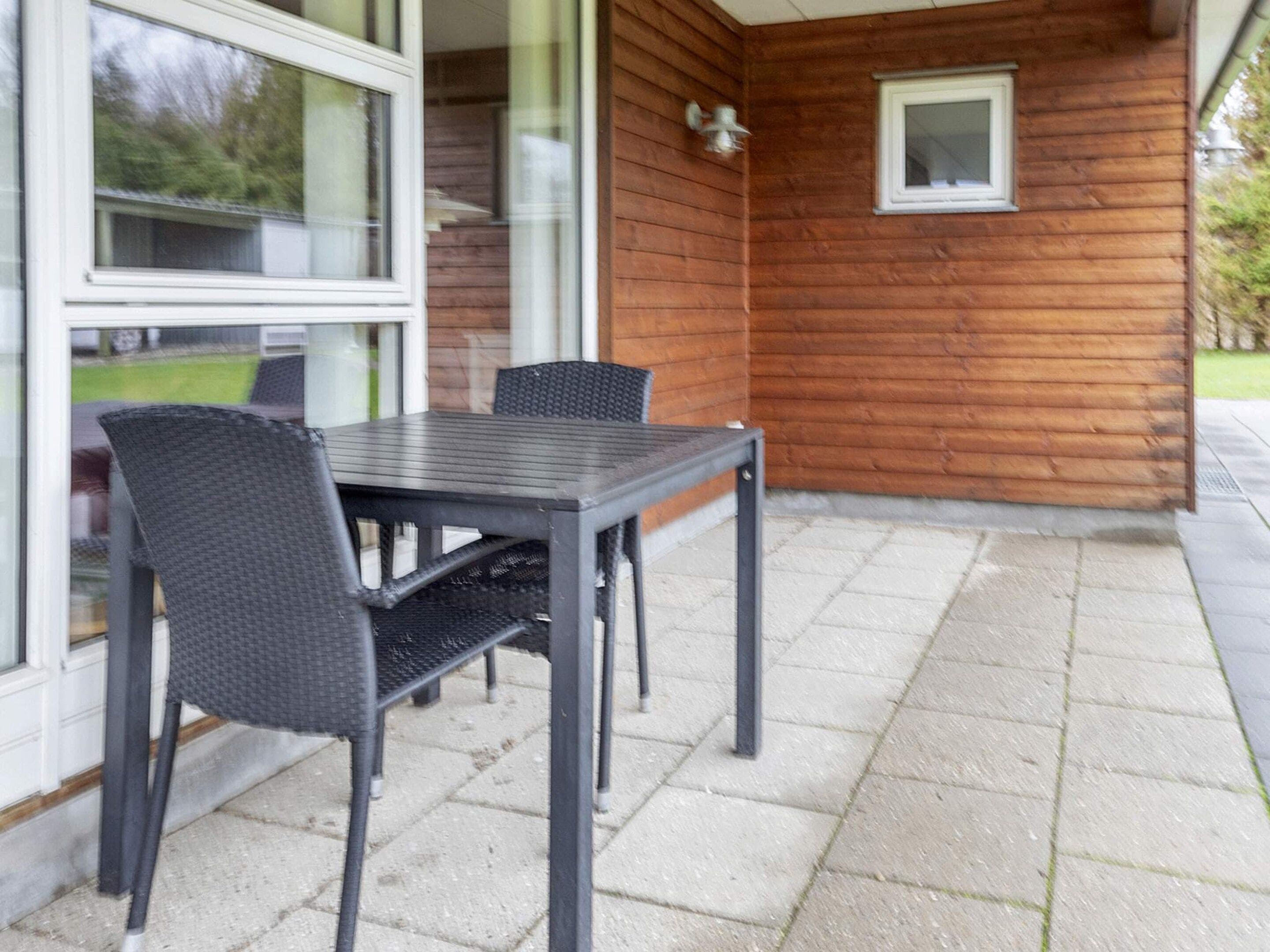 Um pátio externo com mesa e cadeiras, parede de madeira e uma janela.