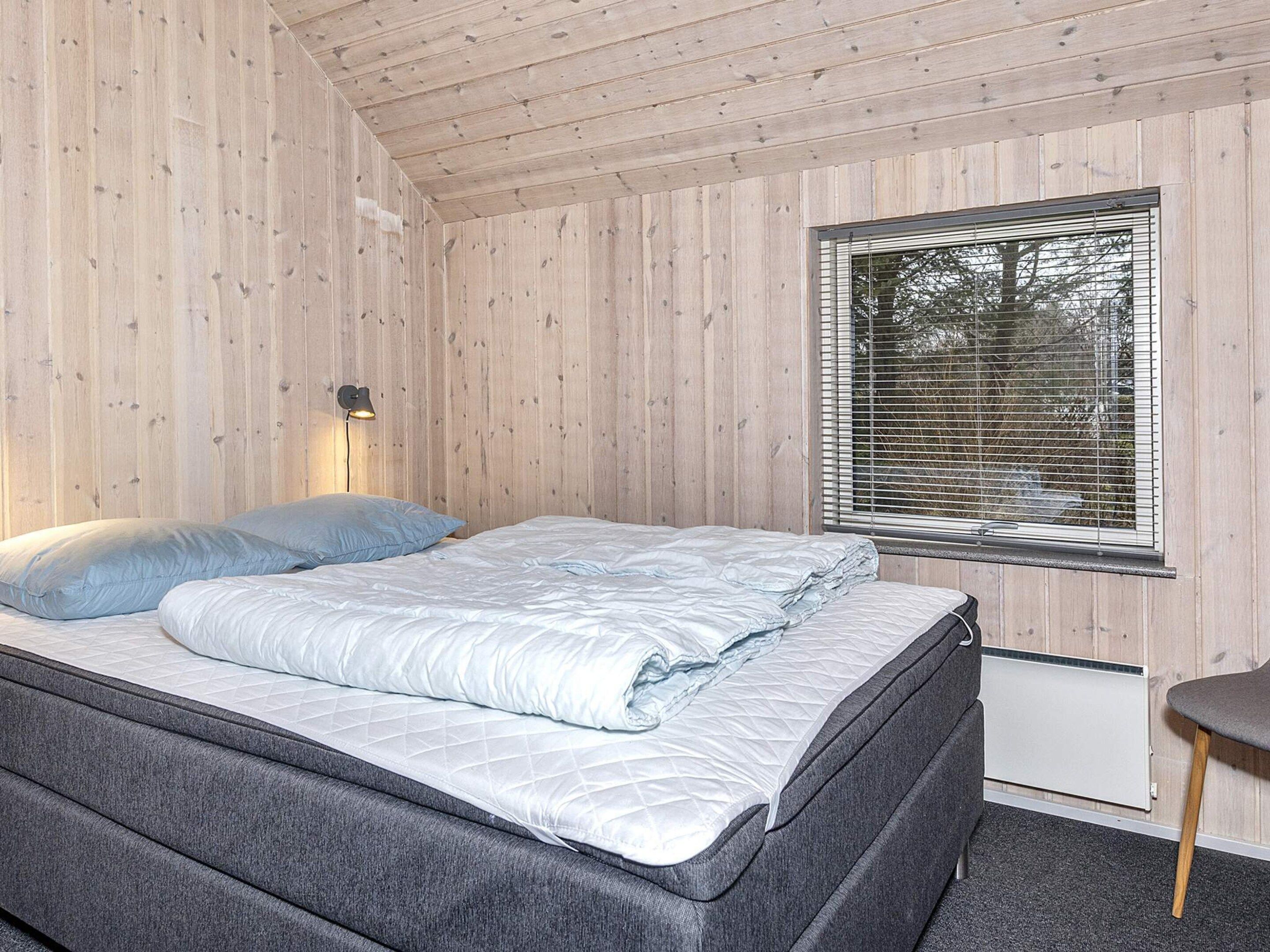 A bedroom with a bed, a window with blinds, and a wall-mounted lamp.