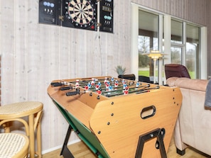 Une table de baby-foot dans une pièce où se trouvent également un jeu de fléchettes et un canapé.
