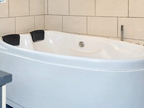 A white bathtub with a single faucet and a control knob, set against a tiled wall.