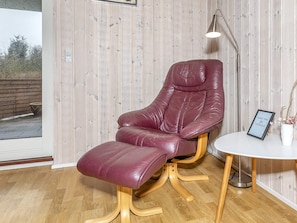 Une pièce comprenant un fauteuil inclinable en cuir, une petite table ronde, un lampadaire et une vue par la fenêtre.