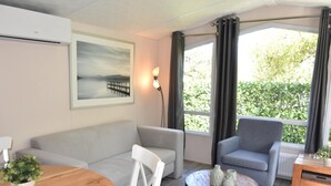Una sala de estar moderna con un sofá gris, una mesa de centro redonda de madera, un sillón gris y un ventanal con cortinas.