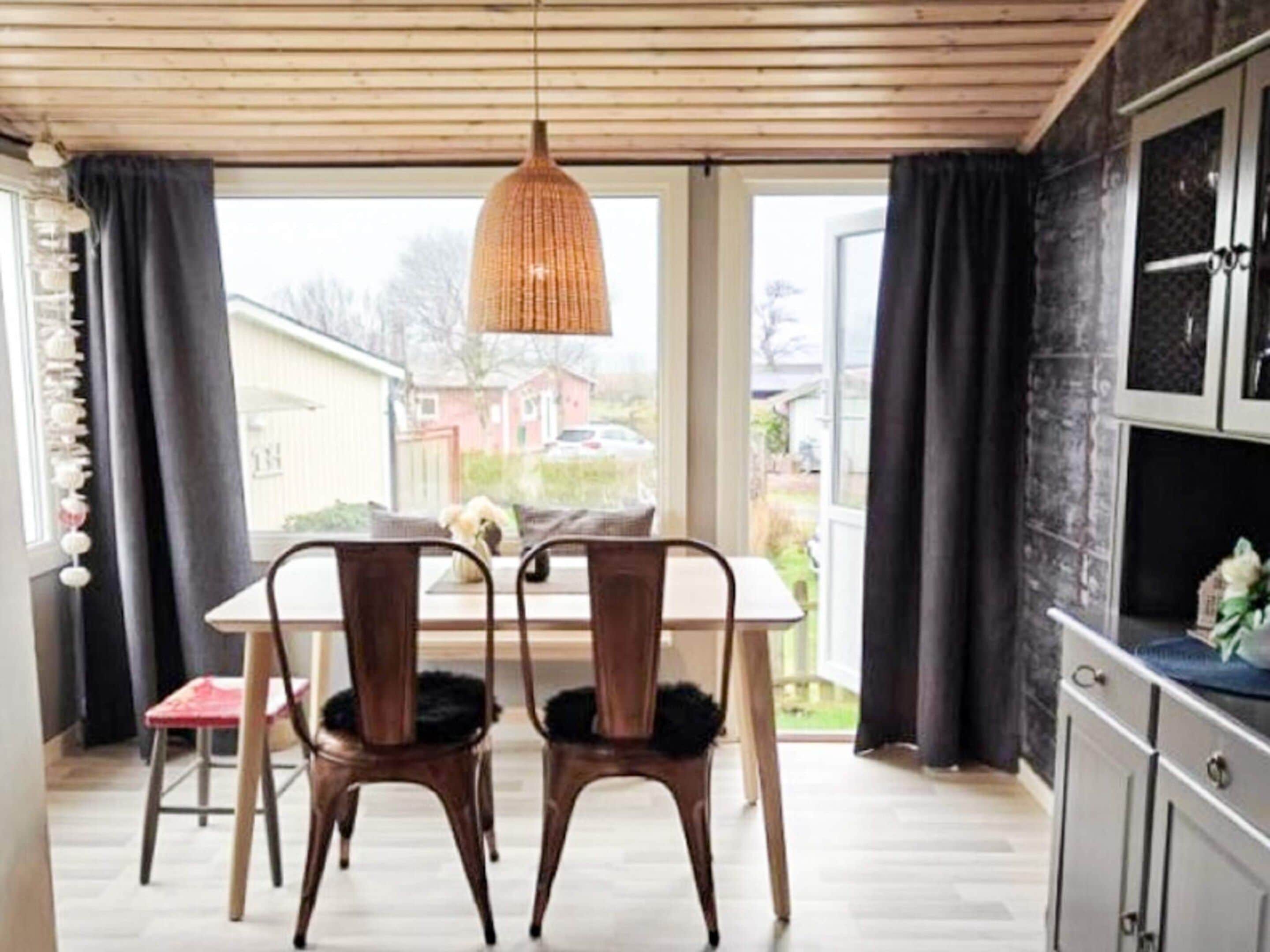 A dining area with a table and chairs, a hanging light fixture, and a view through large windows.