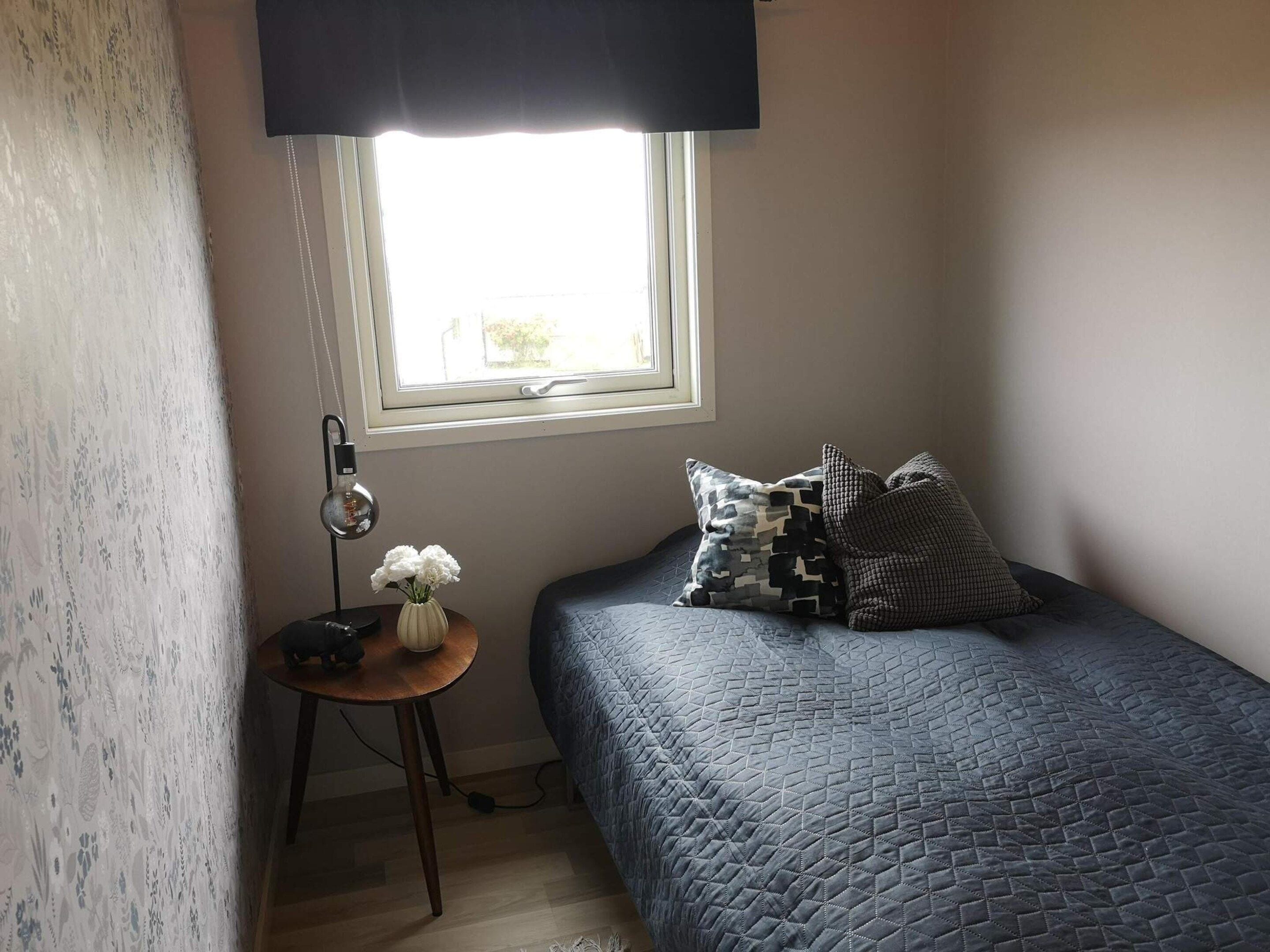 Quarto com uma cama, mesa de cabeceira, luminária e janela.