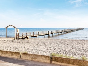 A beach with a wooden pier extending into the sea, a lifeguard hut, and a concrete barrier. - 5 Person Holiday Home in Falkenberg (Falkenberg)