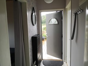 Um corredor com porta para o exterior, um cabideiro, um espelho e um pequeno armário.