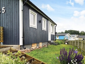 A dark-colored house with a number '5' on the side, a small garden with a wooden bench, and a wooden fence.