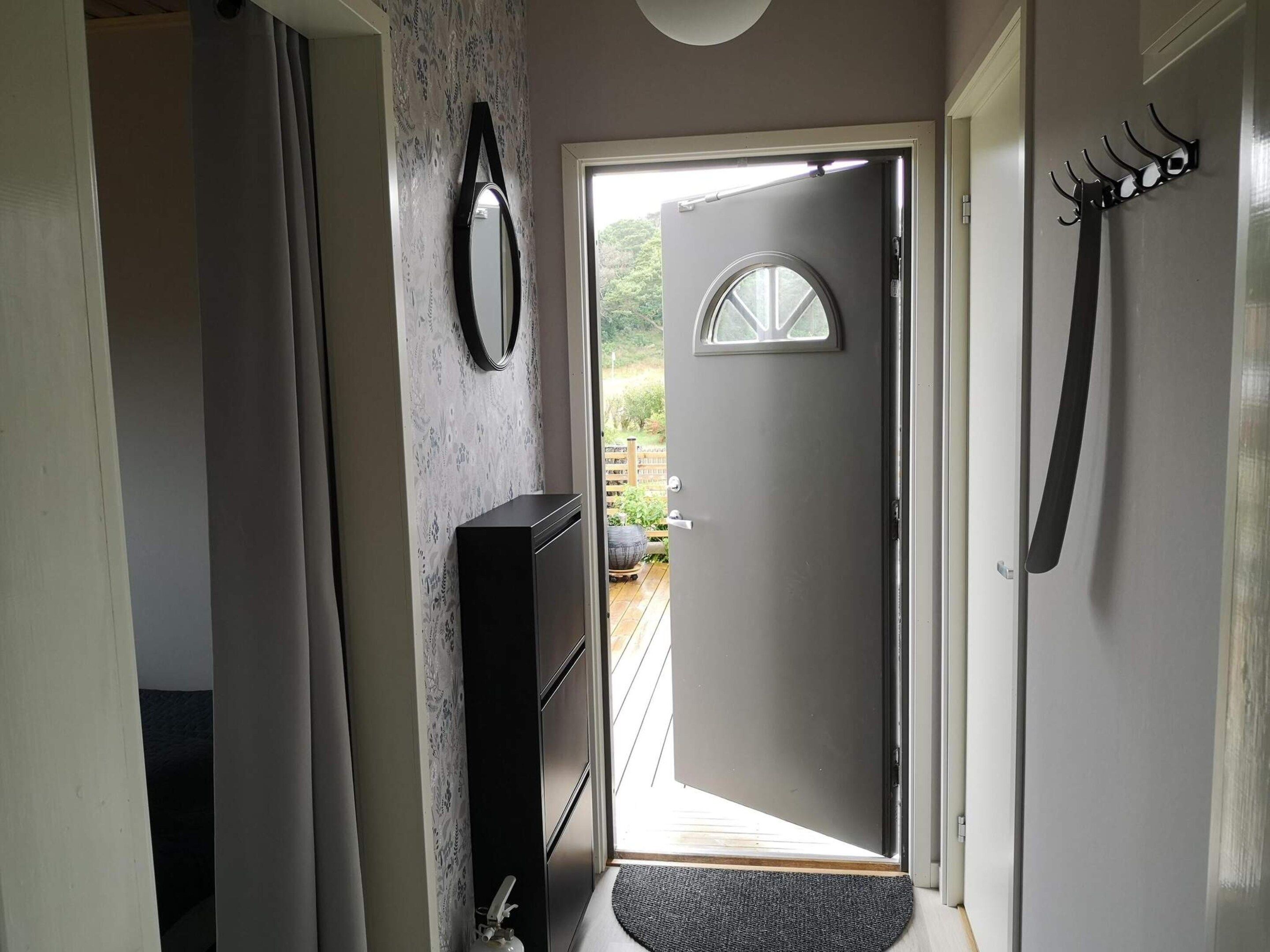 Un couloir avec une porte donnant sur l’extérieur, un porte-manteau et un miroir accroché au mur.