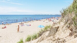 A beach with people sunbathing and swimming, a clear sky, and a distant view of a city skyline. - 5 Person Holiday Home in Falkenberg (Falkenberg)