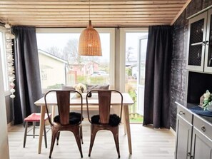 A dining area with a table and chairs, a hanging light fixture, and a view through large windows.