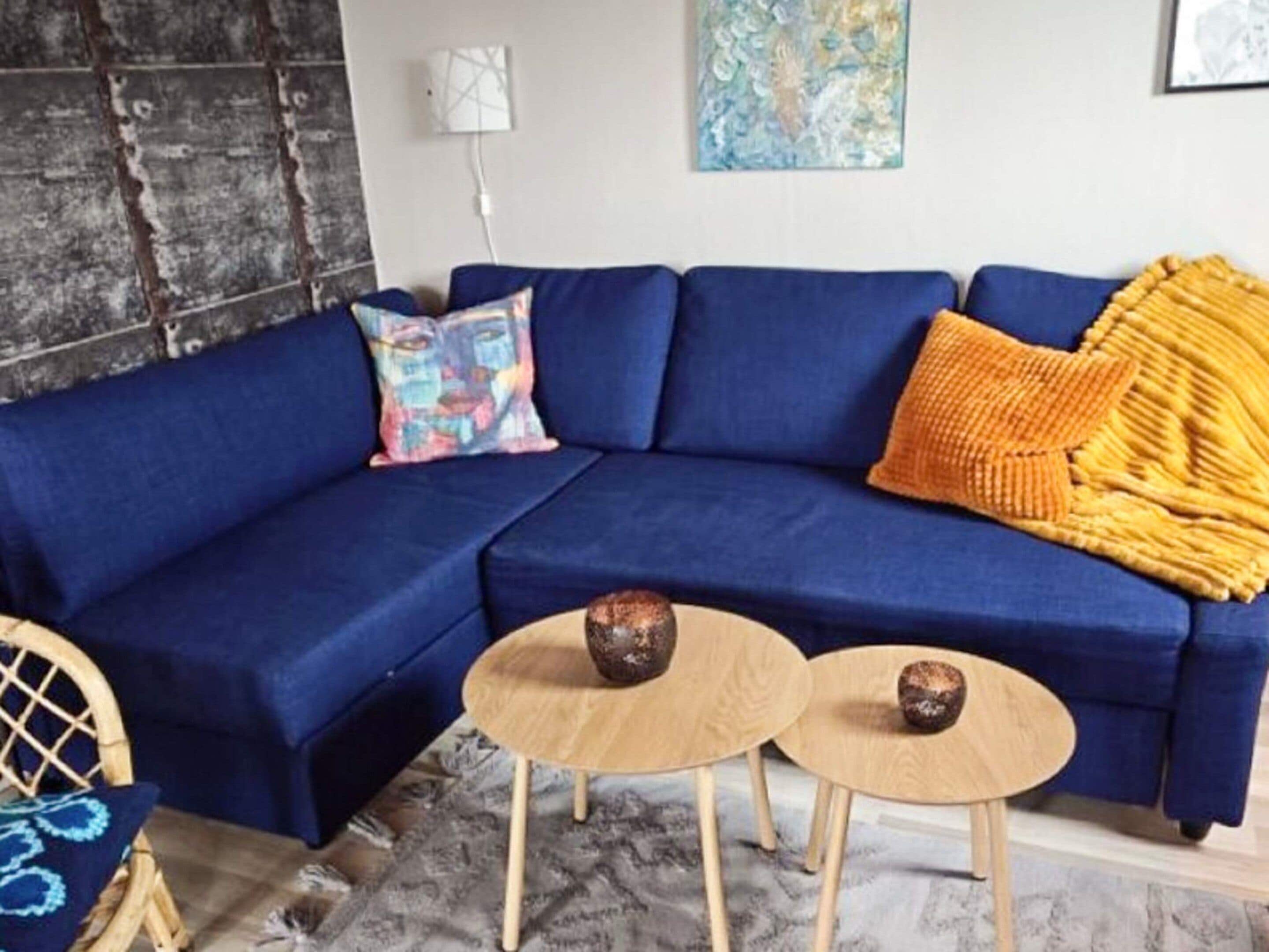 A blue sofa with a colorful pillow, a yellow throw blanket, and two small wooden tables with decorative vases.