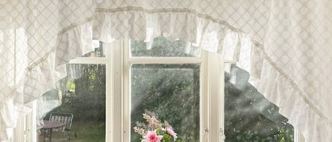 A window with a white frame, lace curtains, and a vase with flowers on the windowsill.