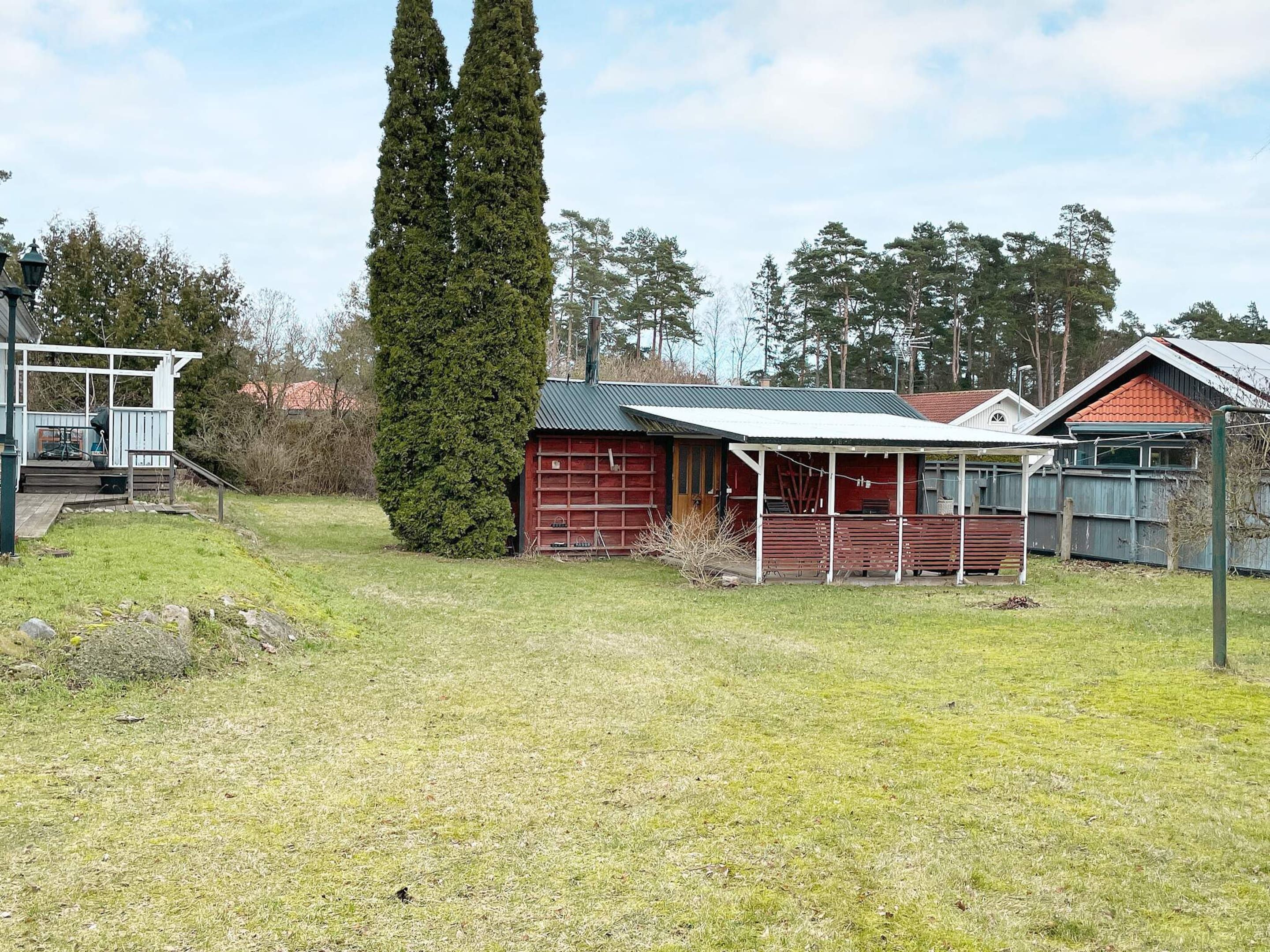 Una vivienda con garaje rojo, un porche cubierto y un alto pino.