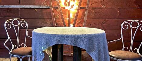 A table with a white tablecloth, two metal chairs with brown cushions, and a decorative light fixture in the background.