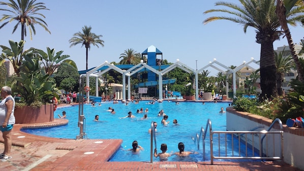A swimming pool with multiple lanes, palm trees, and a water slide structure.