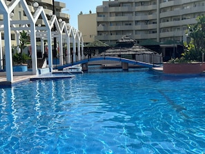 En swimmingpool med en bro, omgivet af bygninger og et overdækket område.