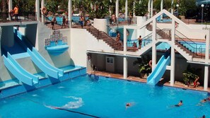 A multi-level pool with slides and stairs, surrounded by palm trees and a clear blue sky. - Beachfront Apartment With Terrace (Benalmádena)