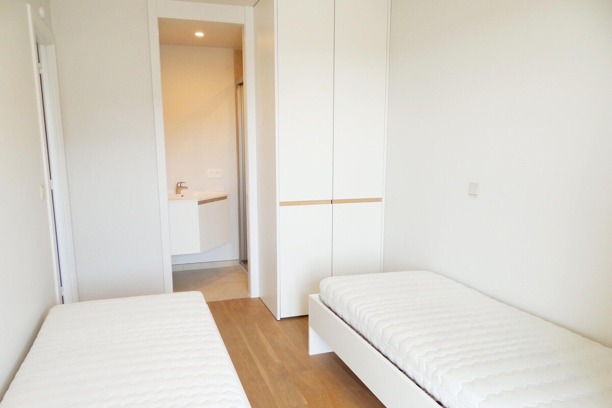 A small, clean room with two single beds, a wooden floor, and white walls.